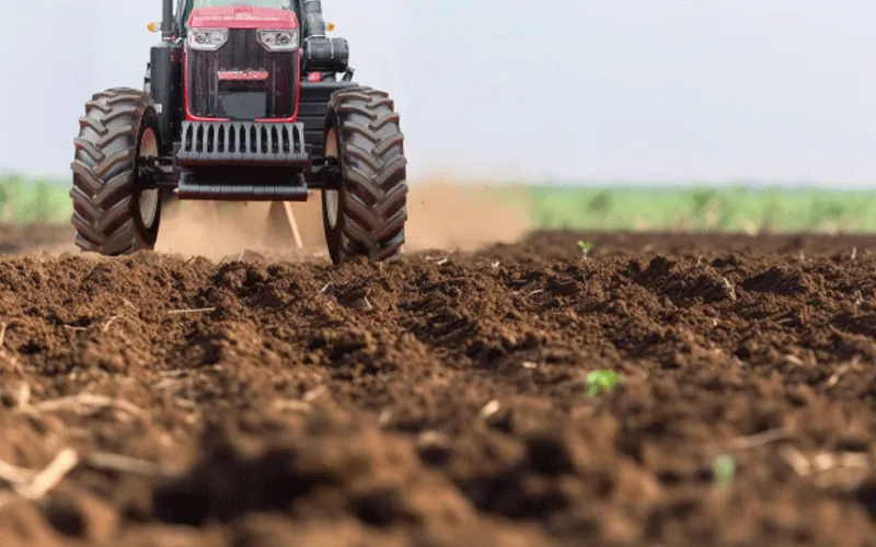 1 Low-angle photo of a red tractor with a black front and large grille plowing a field.